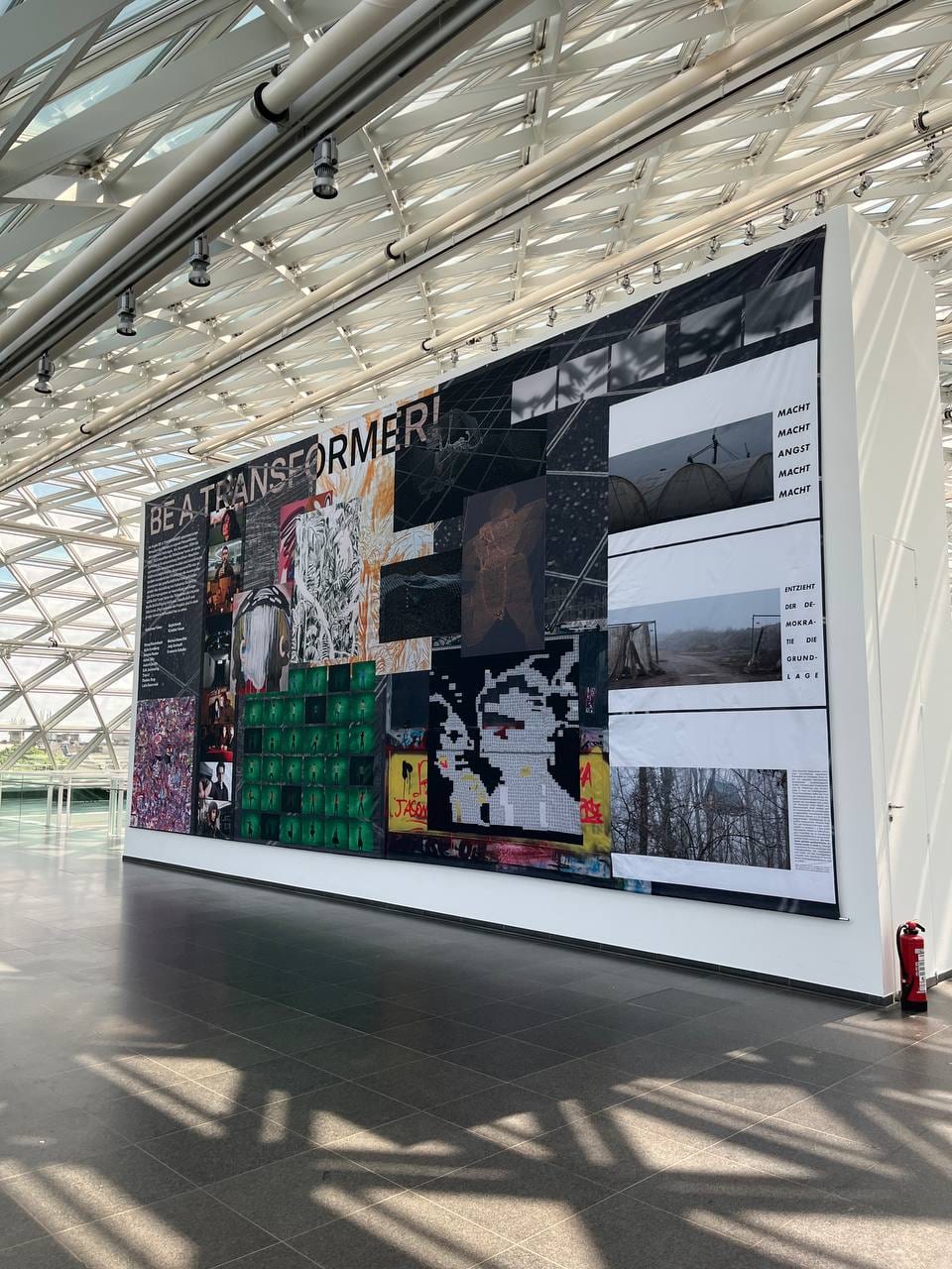 The BE A TRANSFORMER! banner hanging on a free-standing white wall under the glass dome of K21.