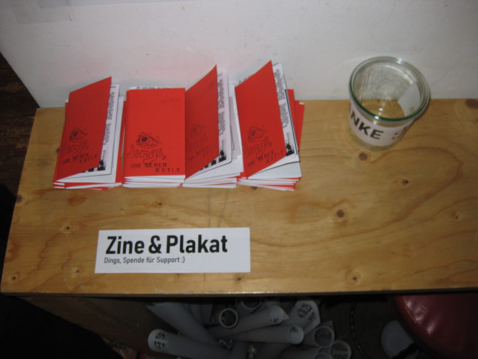 Red zines laid out on a wooden counter next to a sign reading Zine & Plakat.