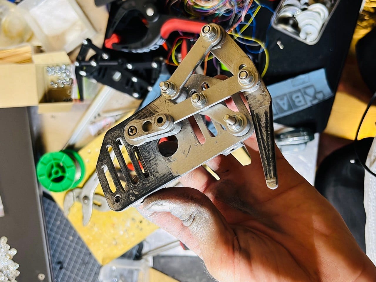 A single leg linkage of the robot held in a paint-stained hand above the workbench.