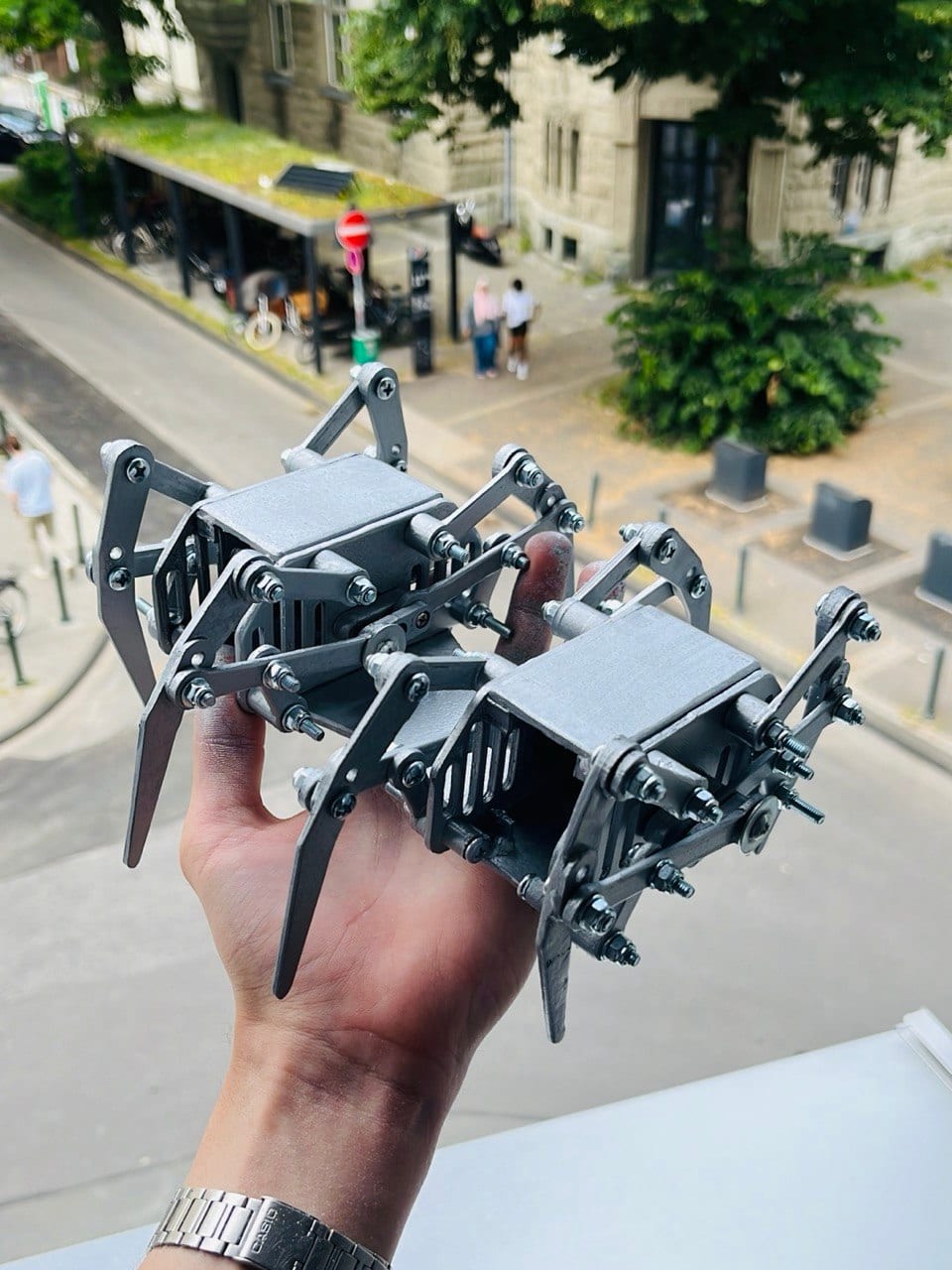 The finished robot, lacquered silver, held in one hand above a street.