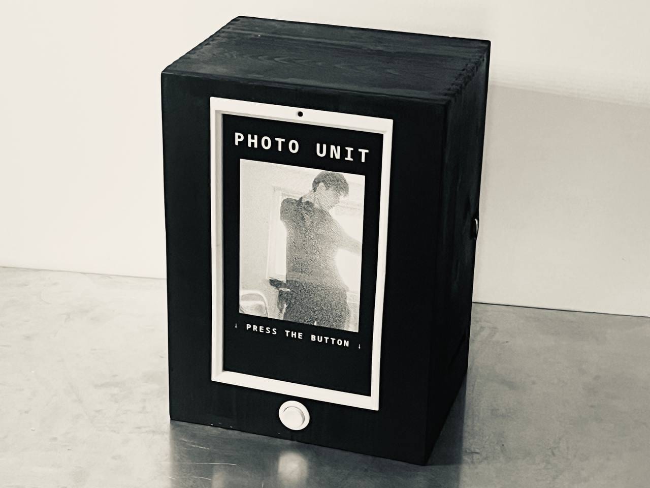 PHOTO UNIT: a black wooden crate with an upright screen in a white frame, showing a live dithered image under the words PHOTO UNIT and PRESS THE BUTTON, a round white button below.