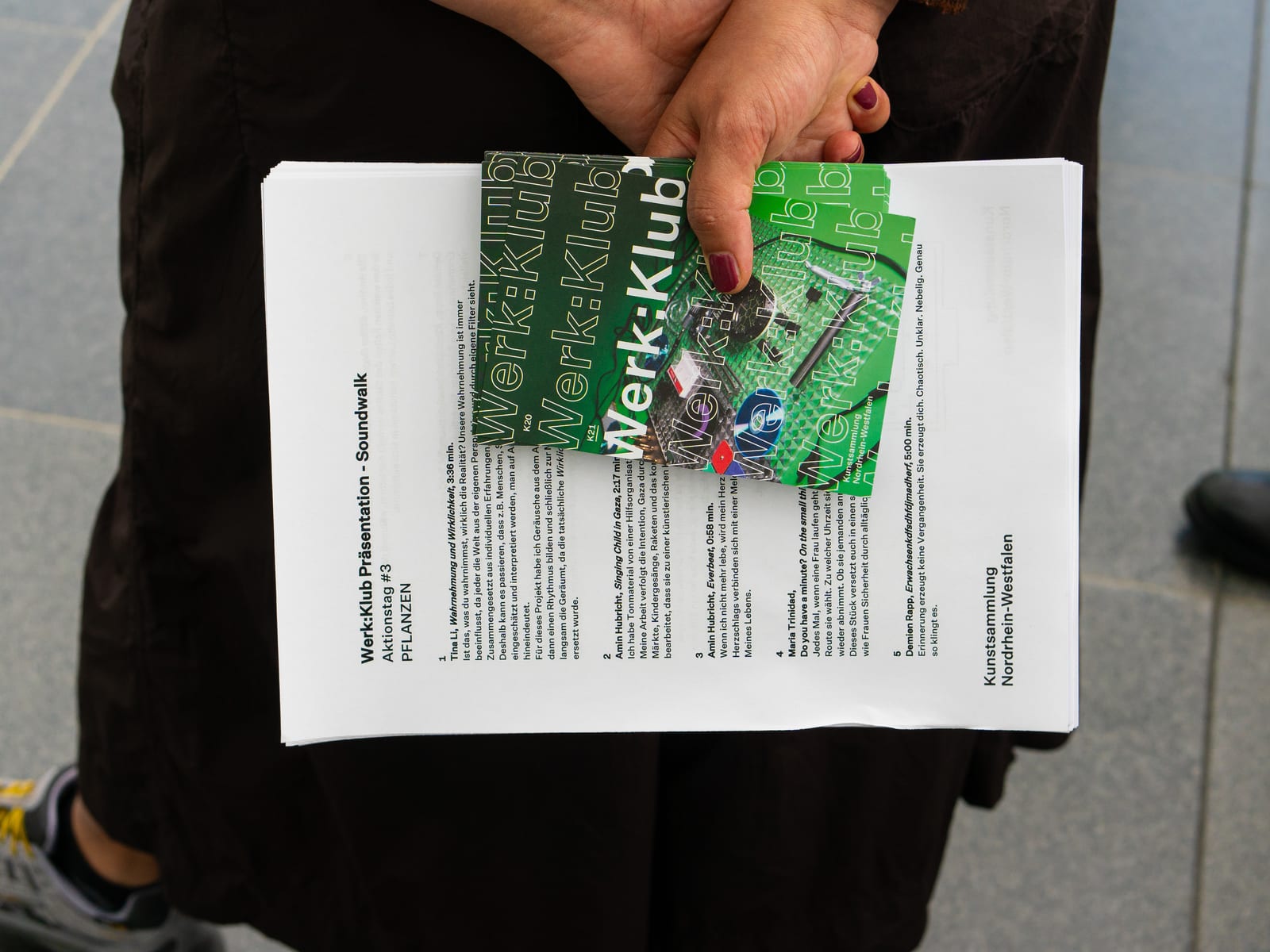 A visitor holds the printed programme of the Soundwalk behind their back.