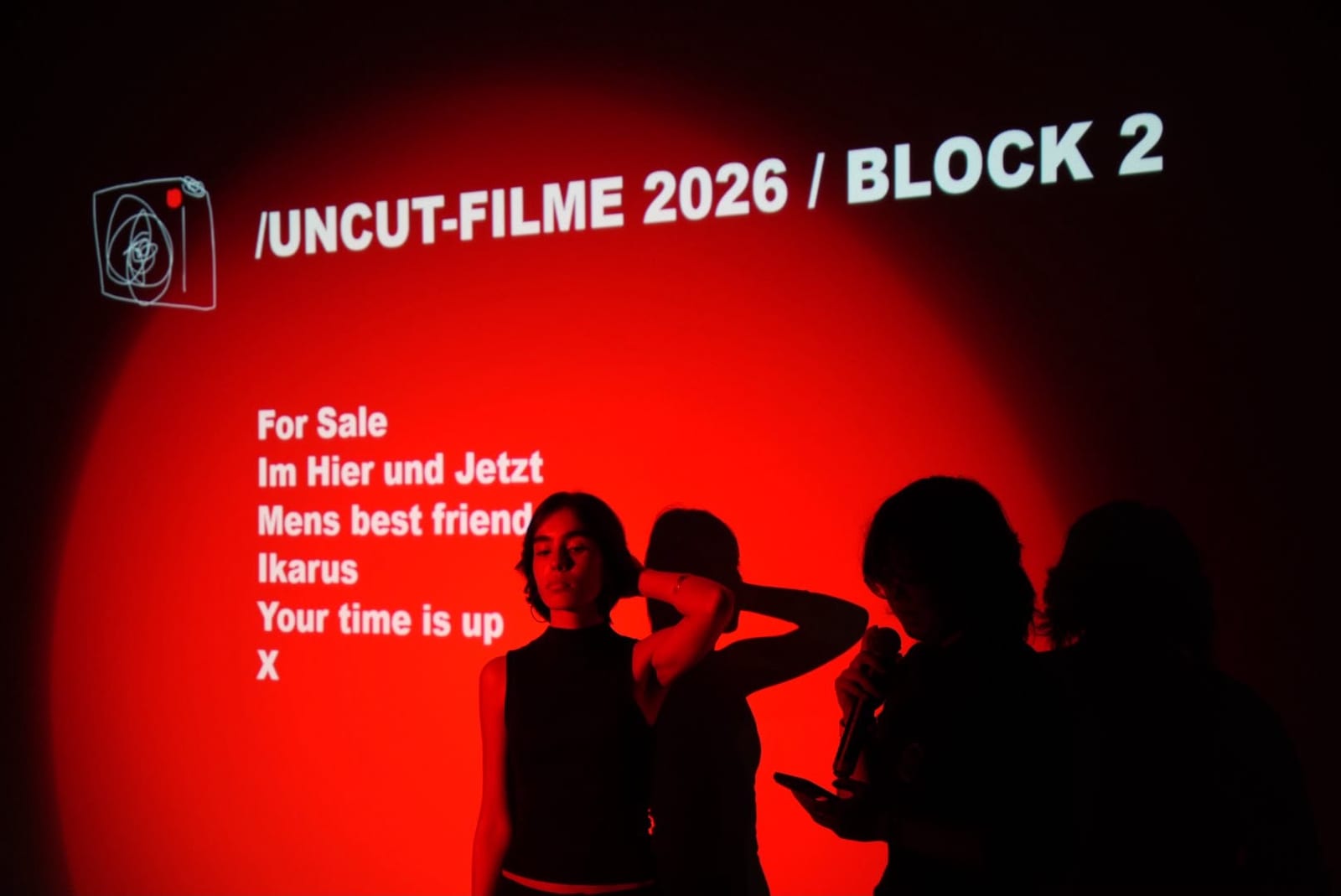 The programme slide UNCUT-FILME 2026 / BLOCK 2 in red light, X last on the list, people with a microphone in front of it.